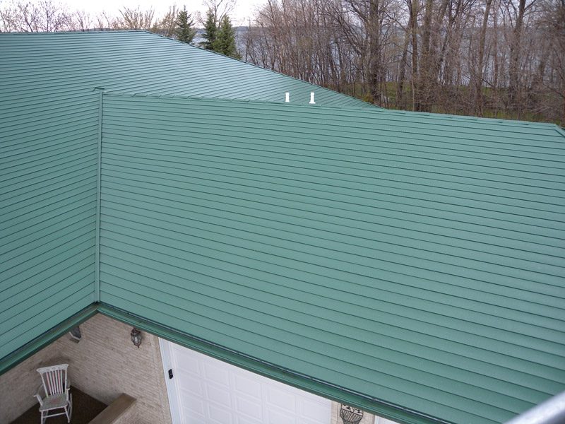 Green ribbed steel roofing panels seen from above, meeting in a valley over an attached garage.