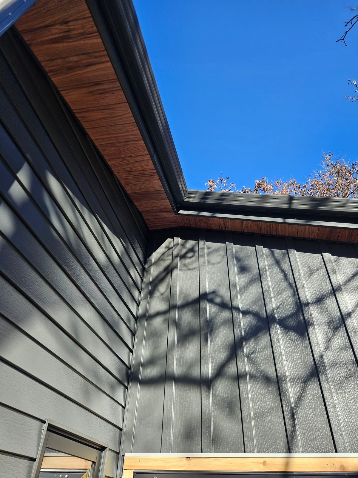 Gray horizontal lap siding meets vertical board-and-batten panels beneath a wood-look soffit.