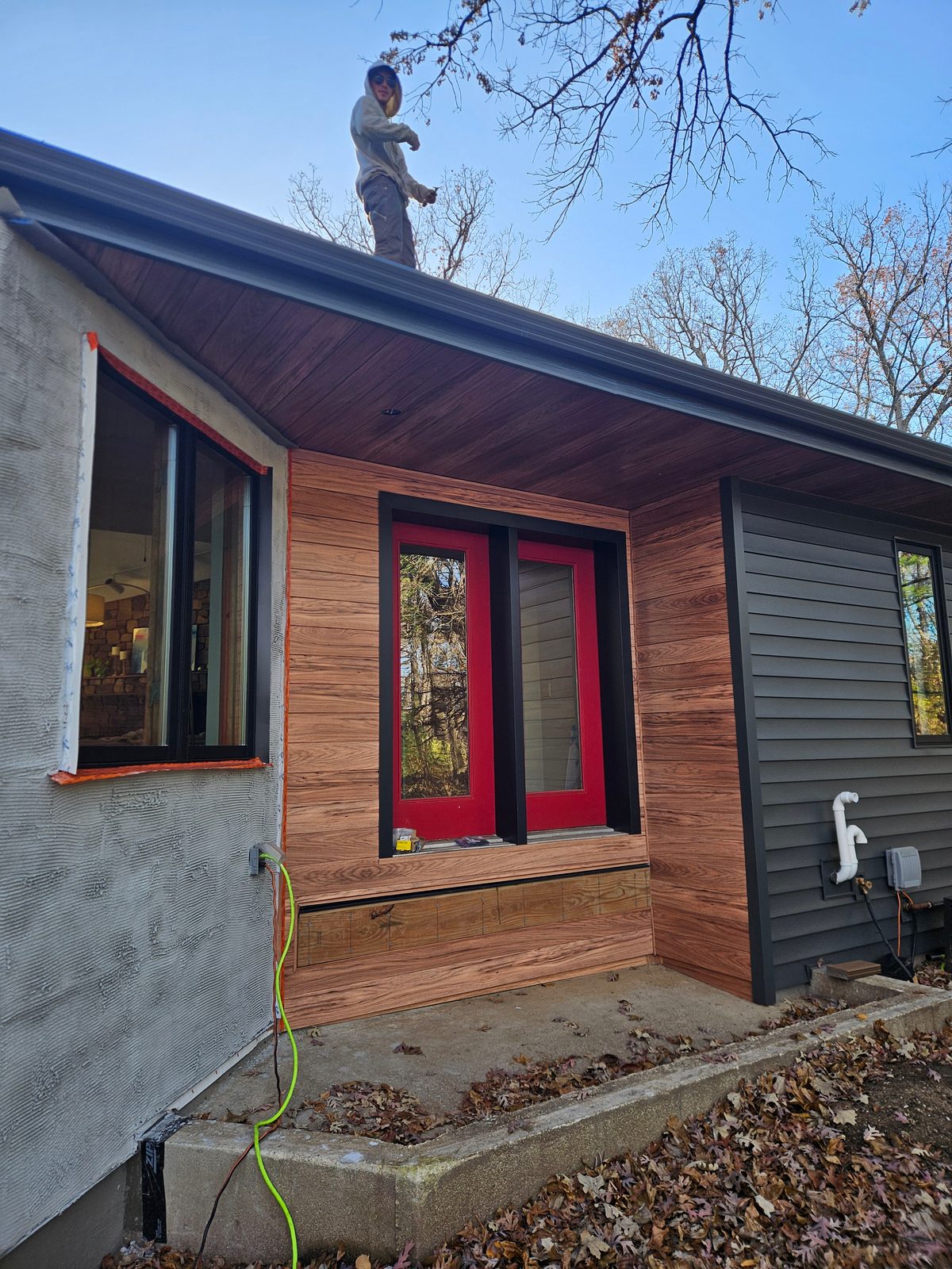 Wood-look steel siding and matching soffit frame a red-trimmed entry beside charcoal lap siding.