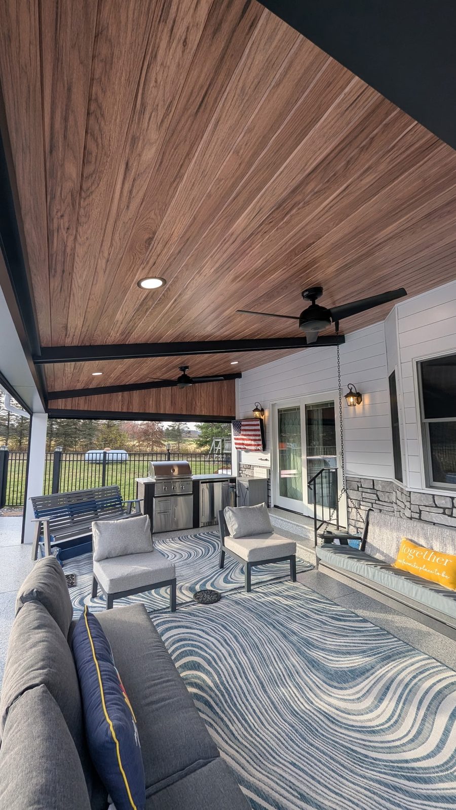 Wood-look steel ceiling panels run between dark beams above a furnished covered porch.