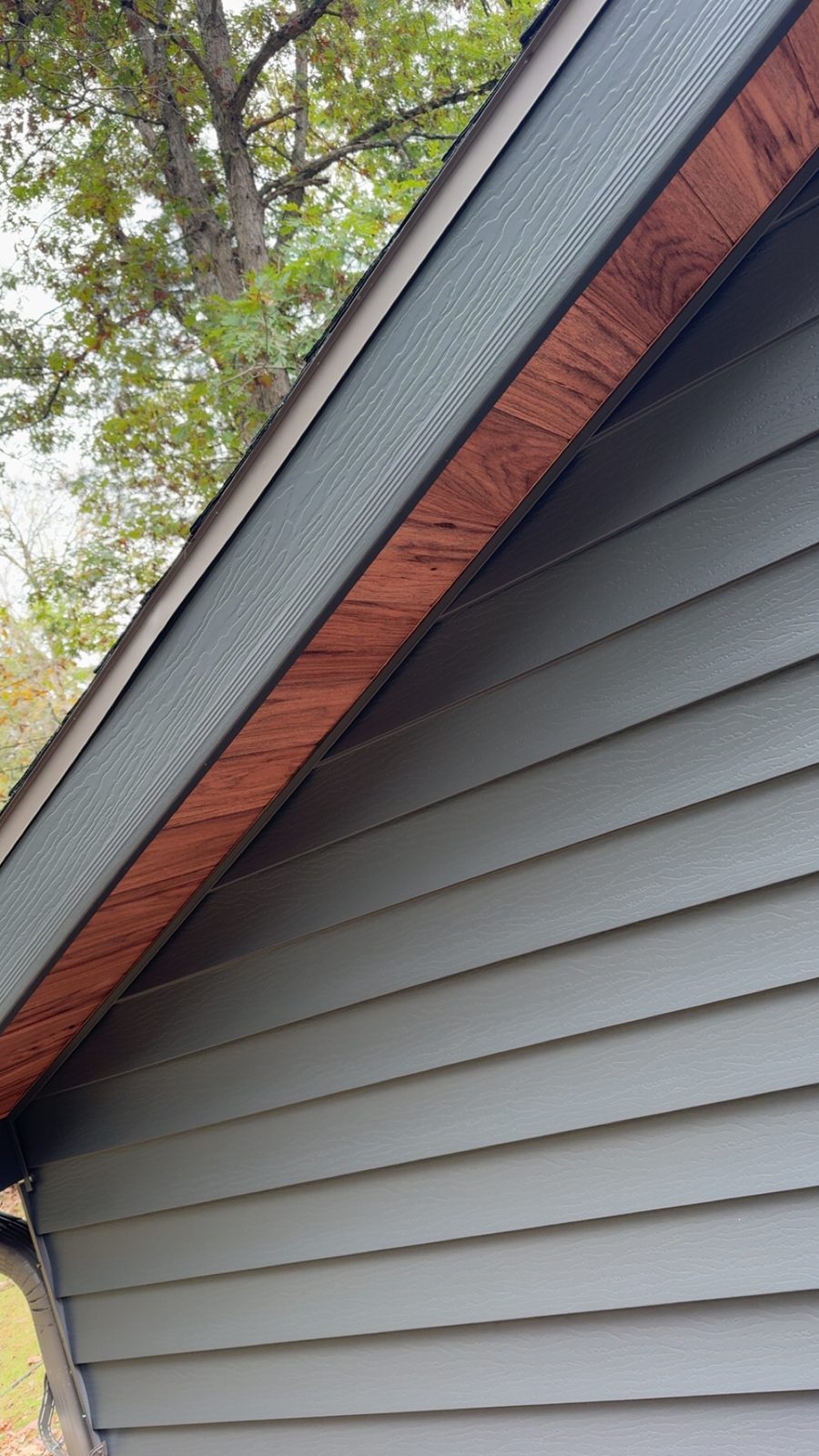 Sage-gray lap siding rises to a gable edged with a wood-look fascia board and dark trim.