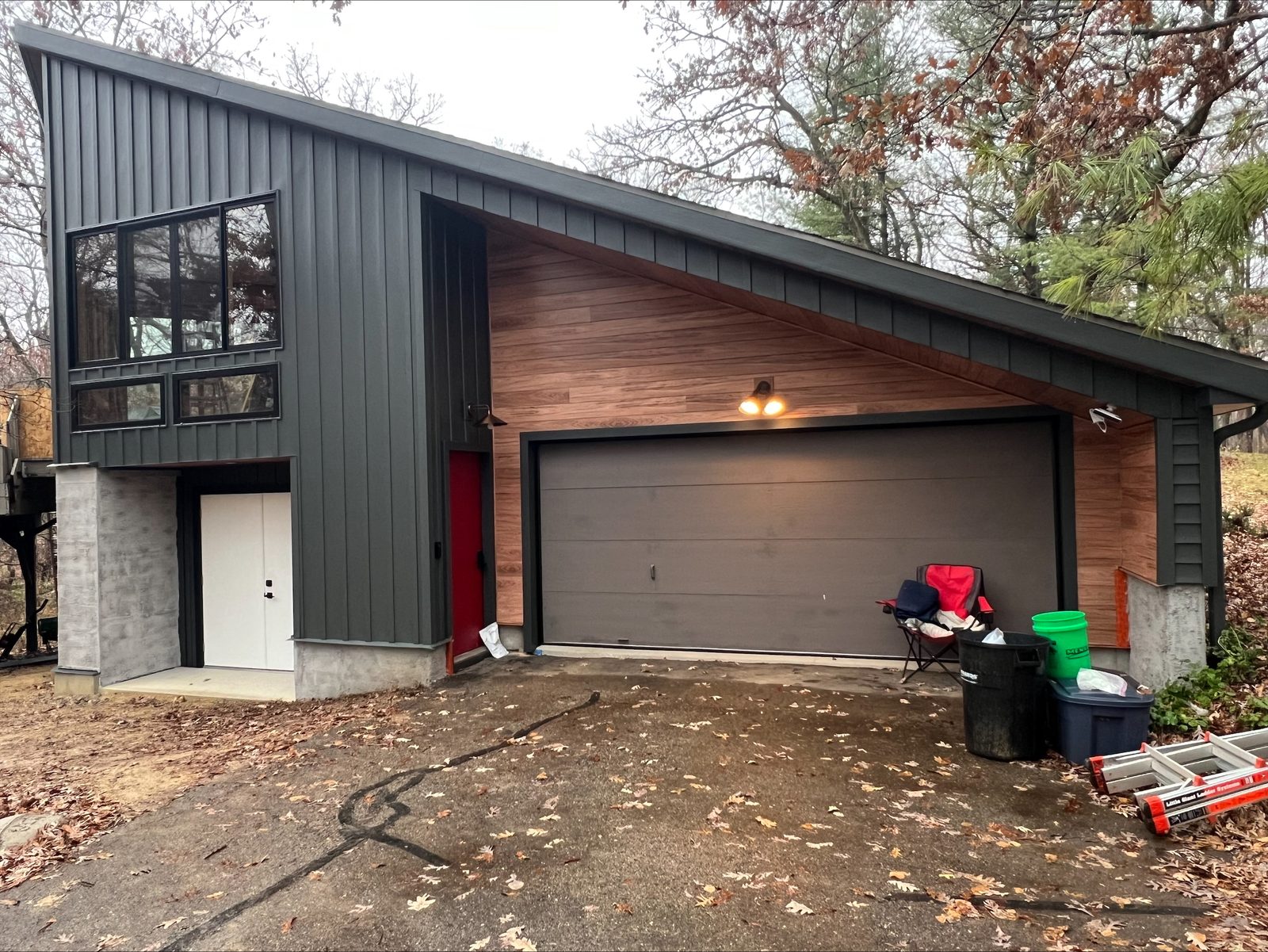 Charcoal board-and-batten steel siding and a wood-look accent panel wrap an angular attached garage.
