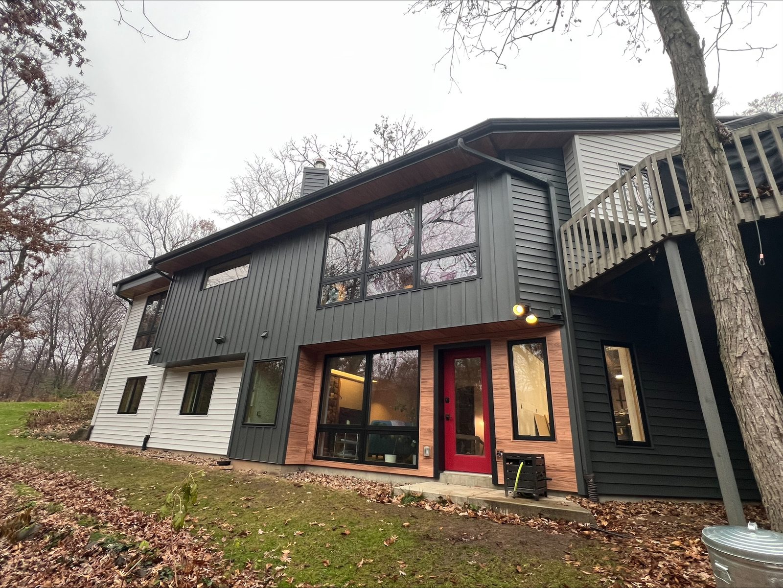Charcoal vertical panels, white lap siding and wood-look accents clad a split-level home on a wooded lot.