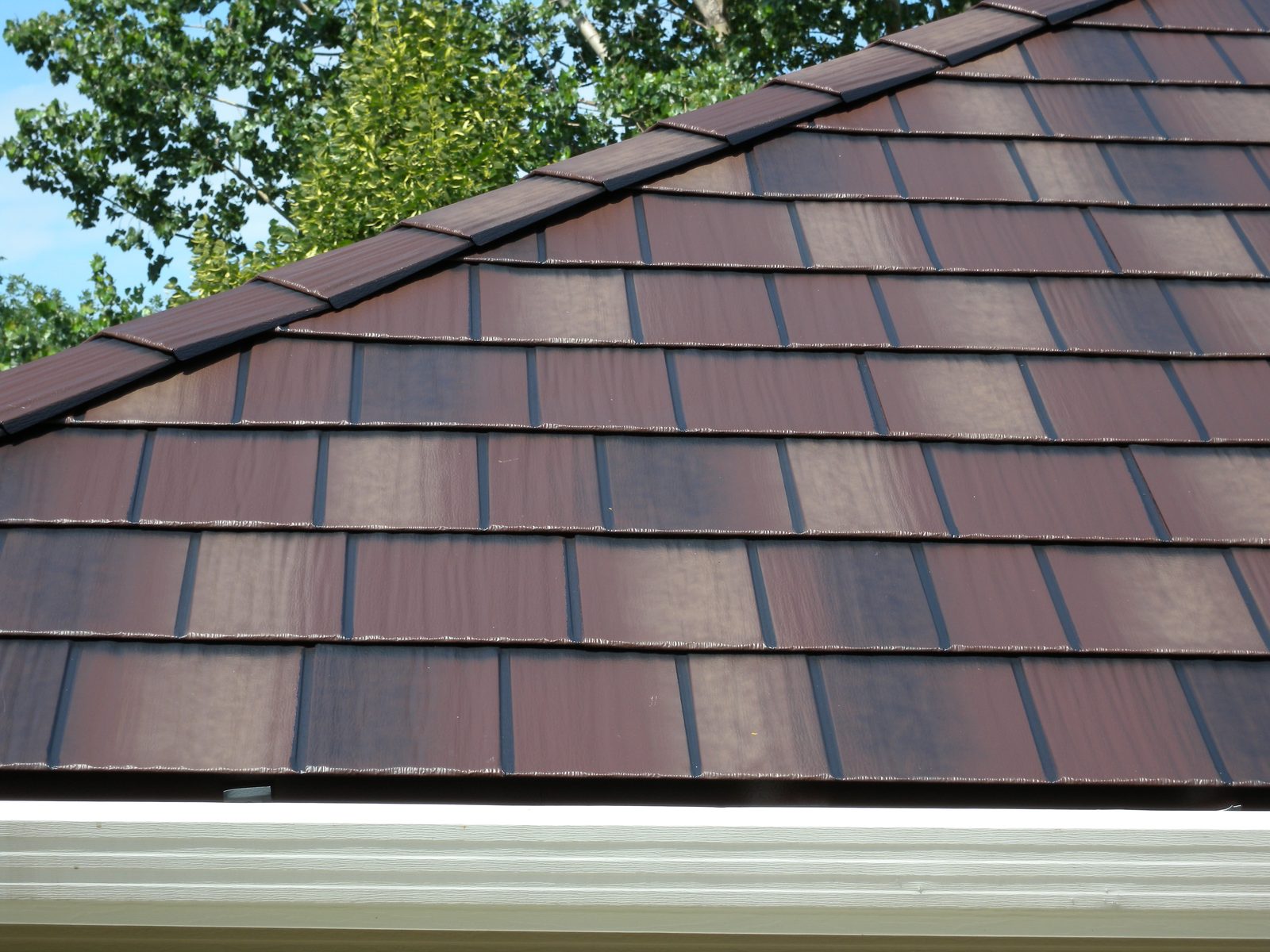 Close view of overlapping brown steel shakes running down a slope toward a white gutter.