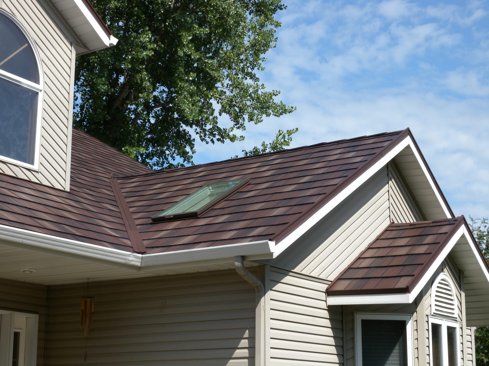 A skylight is set into a brown steel shake roof beside a small gabled dormer.