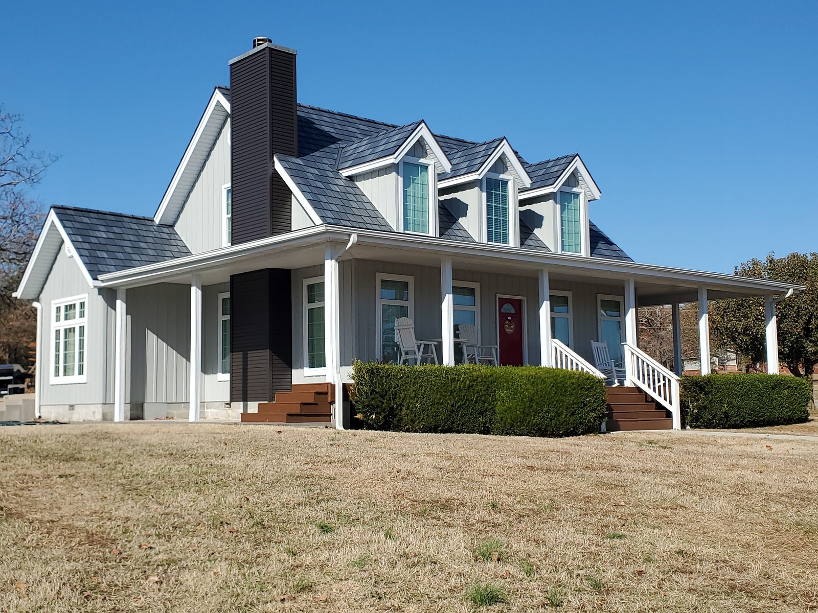 Gray steel shake roofing tops a two-story farmhouse with dormers and a wraparound porch.