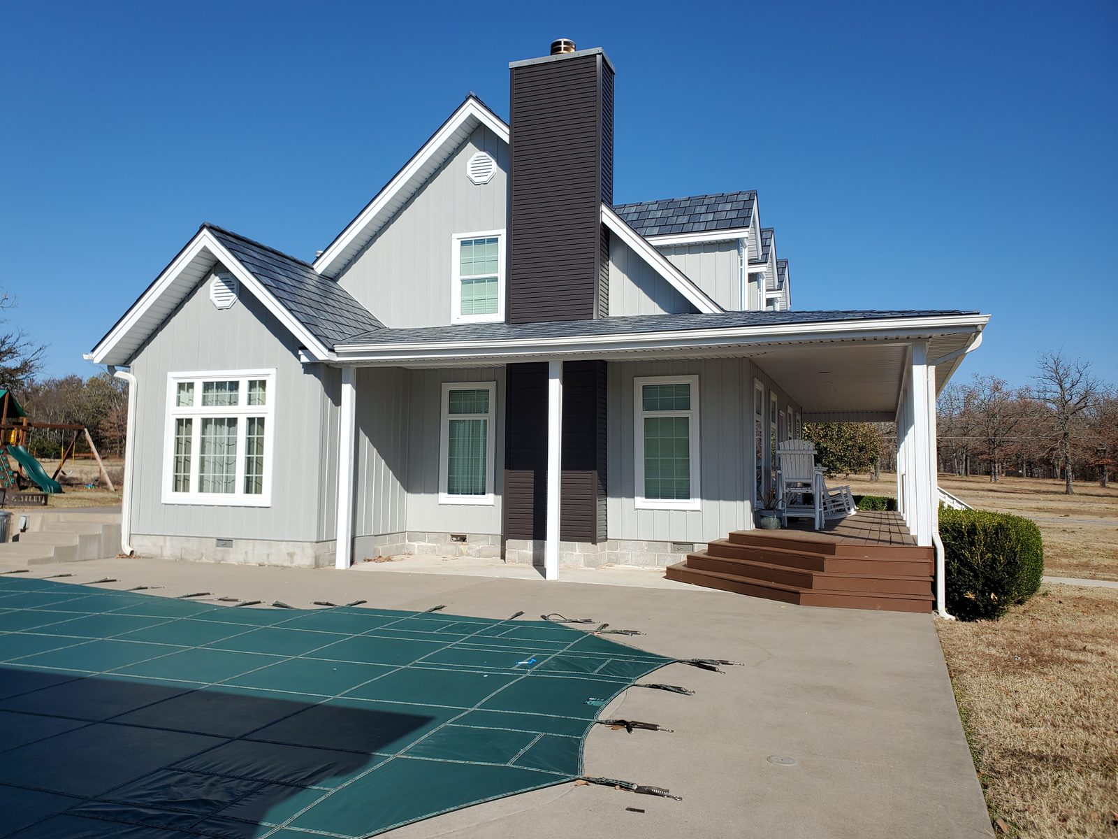 A gray steel shake roof on a farmhouse seen past a covered swimming pool in the side yard.