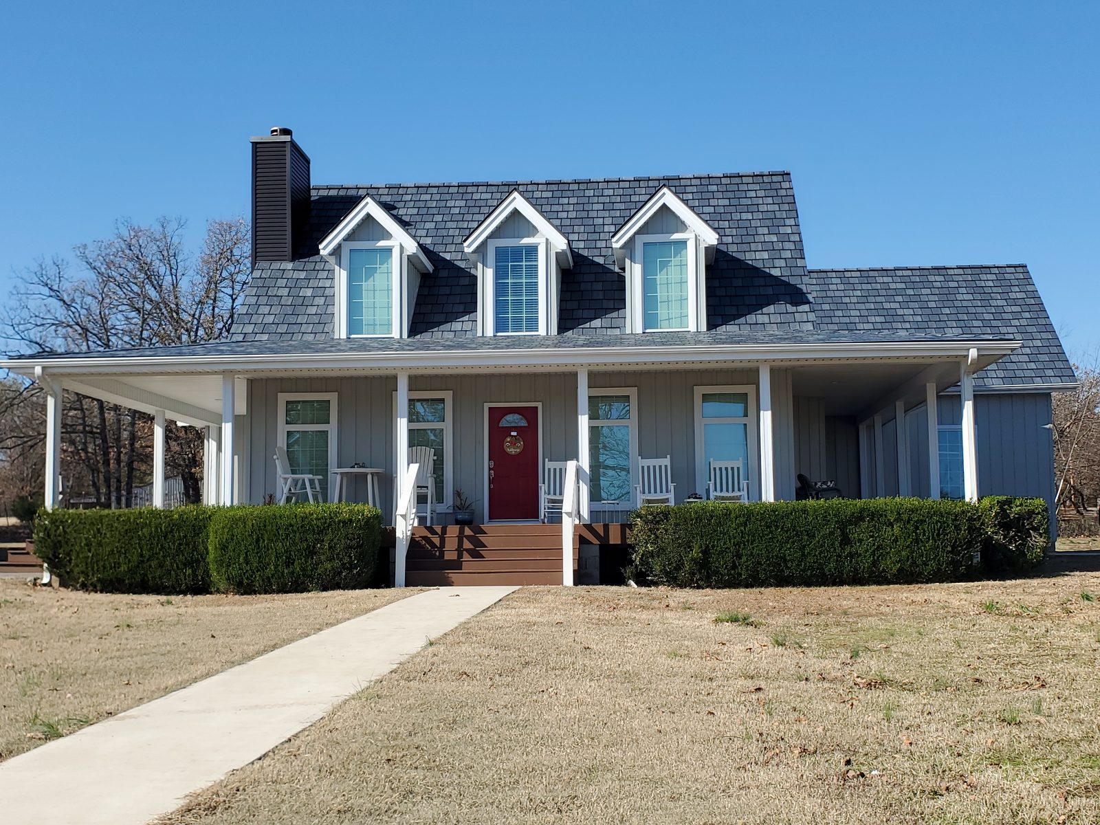 A front walk leads to a farmhouse with gray steel shake roofing and a red front door.