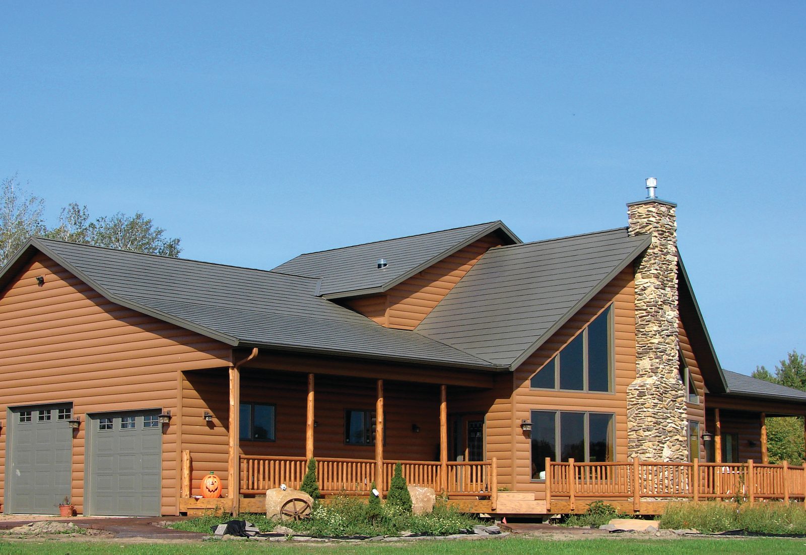 A dark green steel roof spans a log-sided home with a tall stone chimney and covered porch.