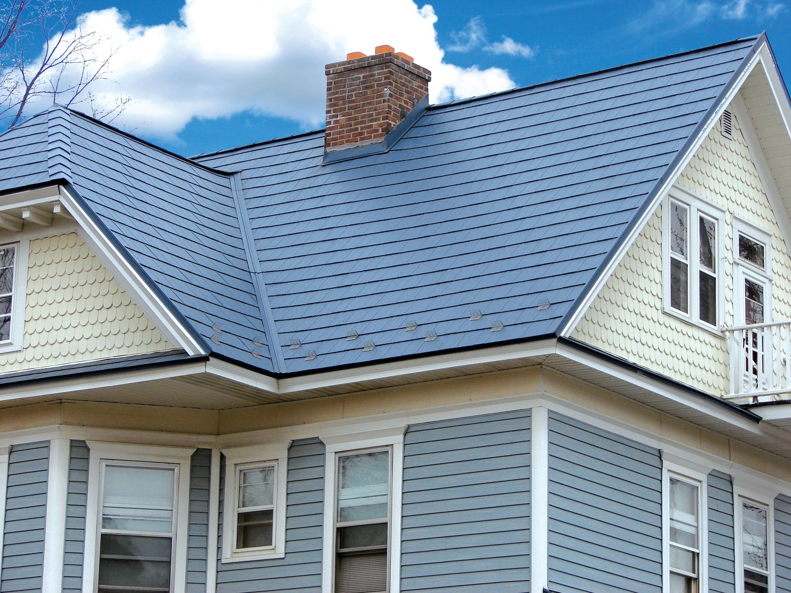 Blue steel shake roofing tops an older home with pale yellow scalloped shingles and blue lap siding.