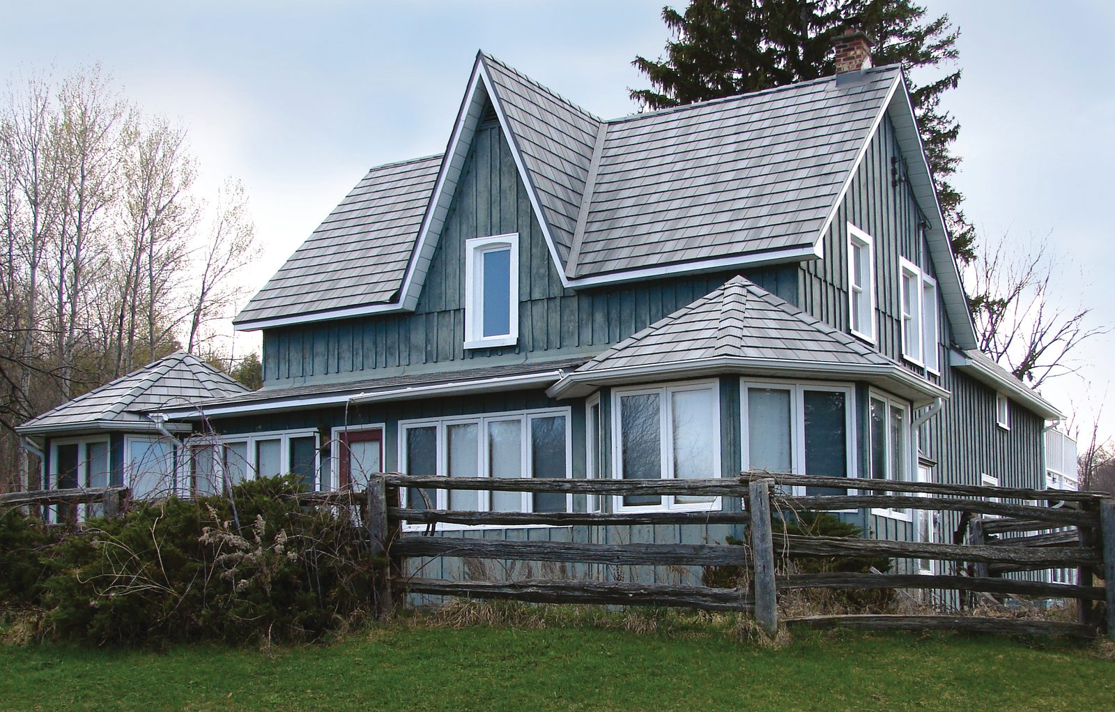 Gray steel shake roofing covers the steep gables of an older home clad in green board-and-batten.