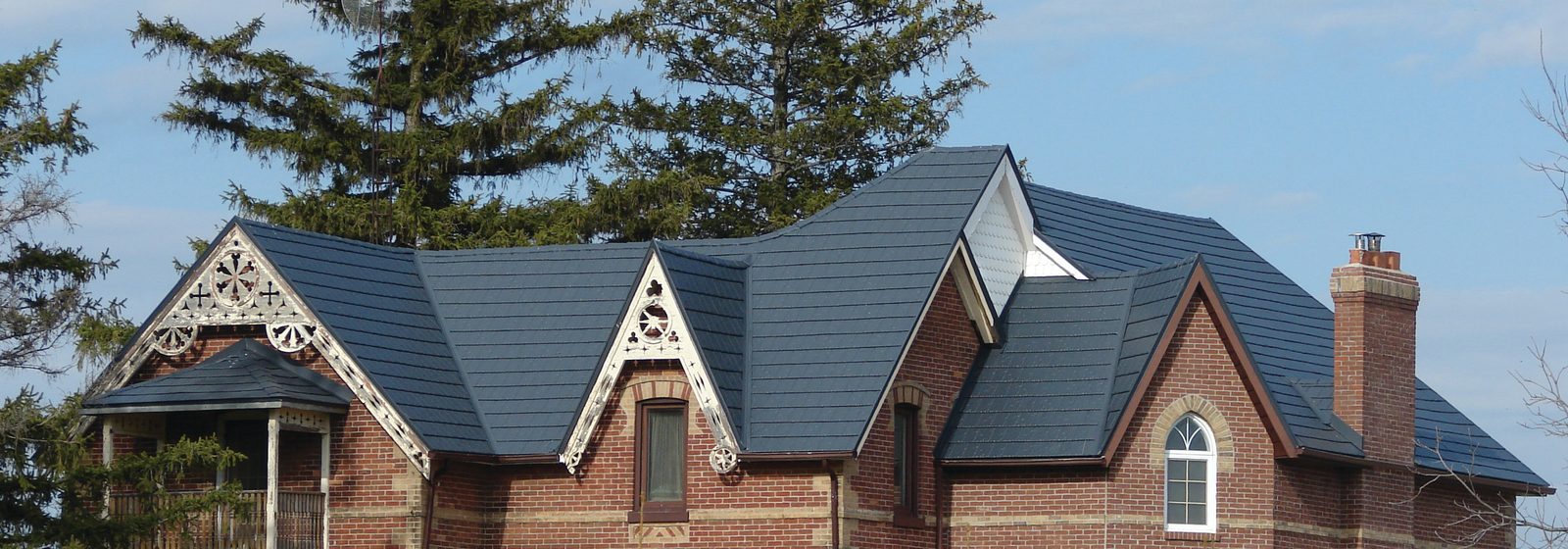 Dark blue steel shake roofing spans the gables of an ornate brick home with decorative bargeboards.
