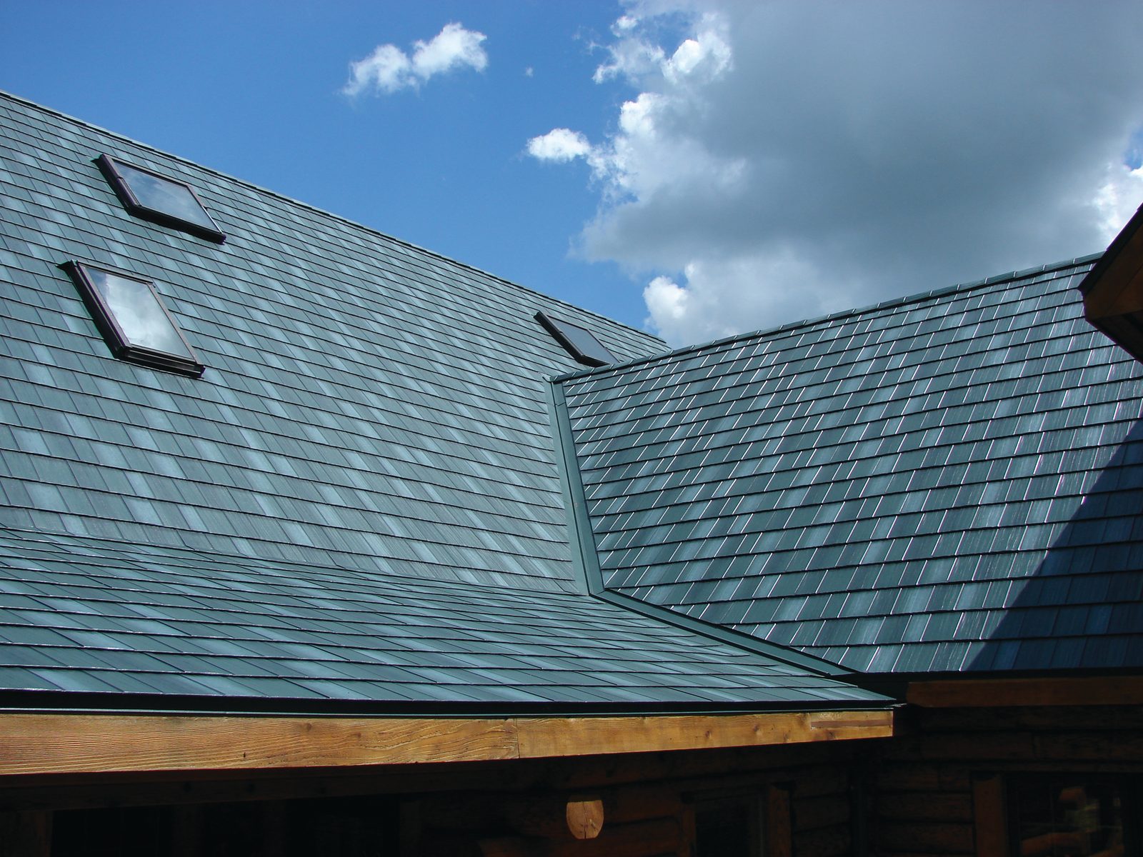Teal steel shake roofing meets at a valley with two skylights above exposed timber rafter tails.