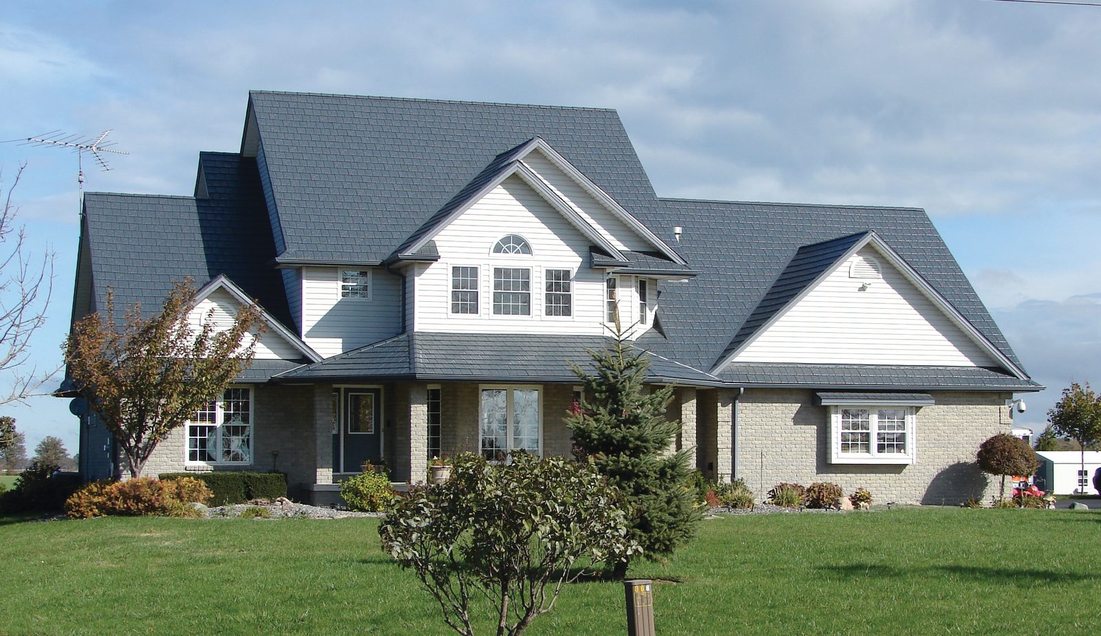Gray steel shake roofing covers the many gables of a two-story home with pale brick and white siding.