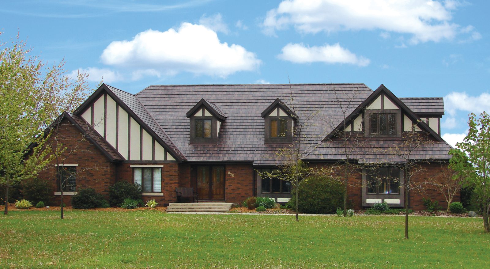 Gray steel shake roofing tops a long Tudor-style brick home with dark half-timbering and dormers.