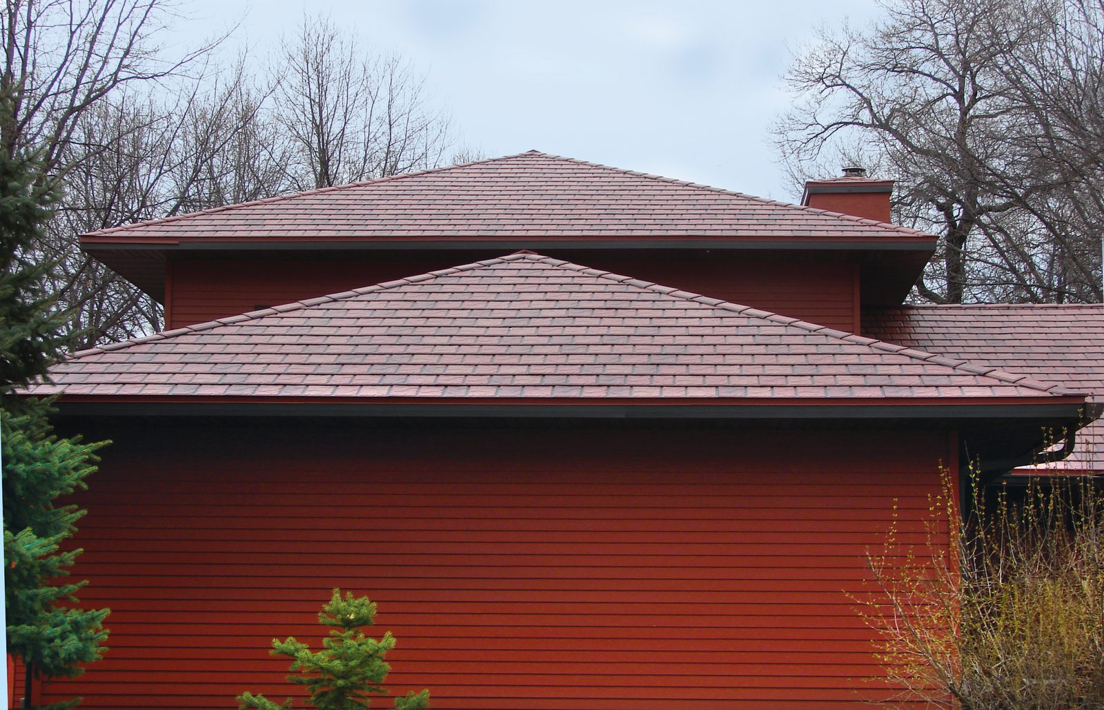 Red slate-look steel roofing covers stacked hip roofs above a deep red lap-sided building.