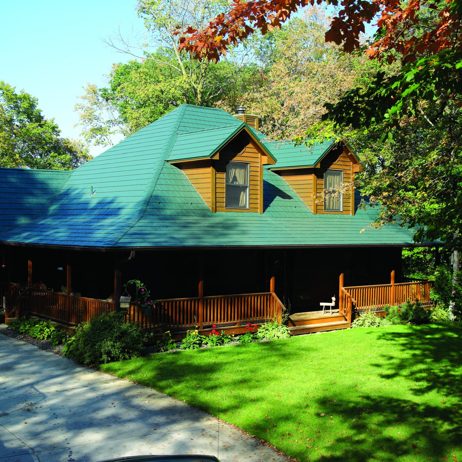 Green slate-look steel roofing covers a log home with two dormers and a wraparound covered porch.
