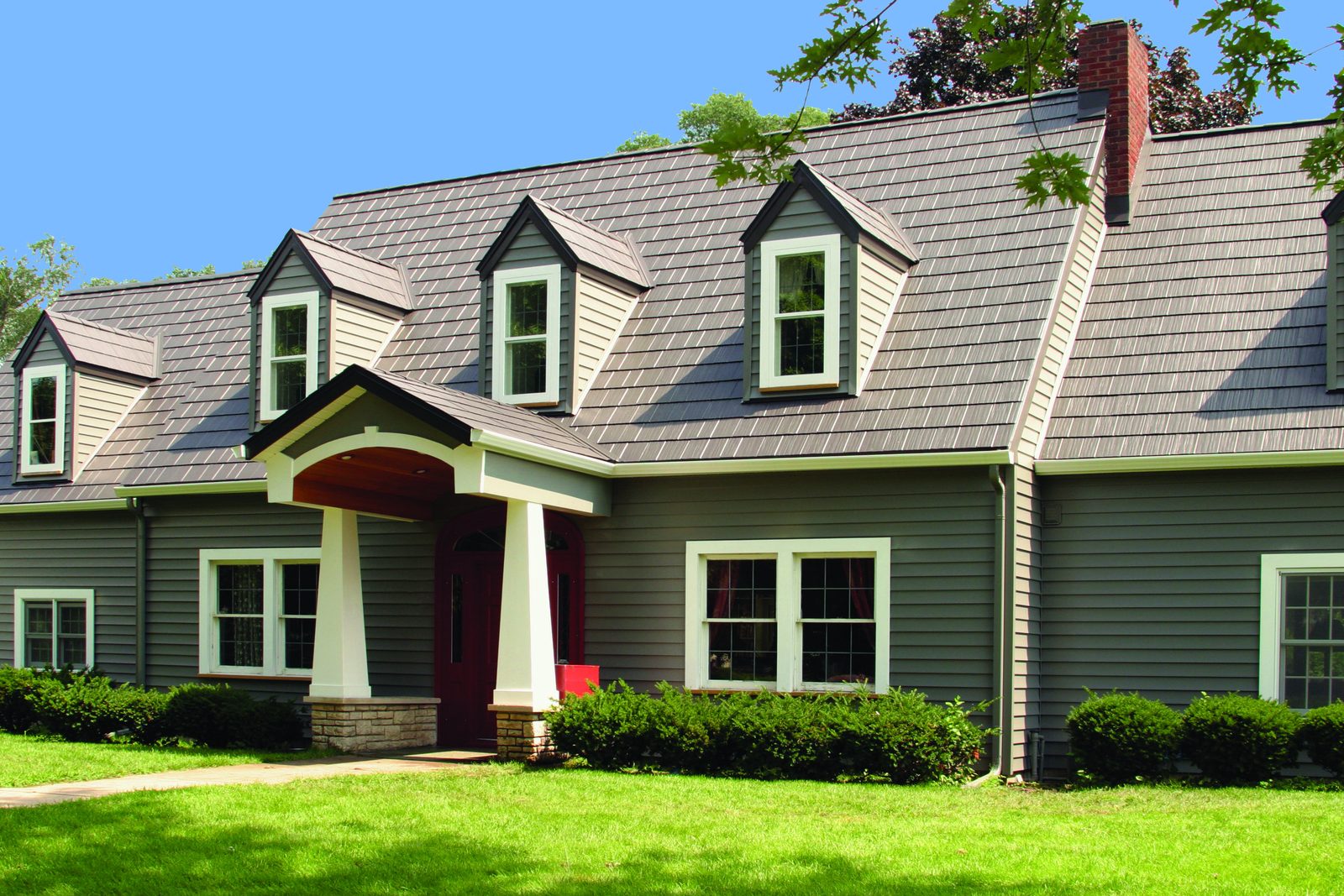 Brown-gray steel shake roofing covers a gray cape-style home with four dormers and a red door.