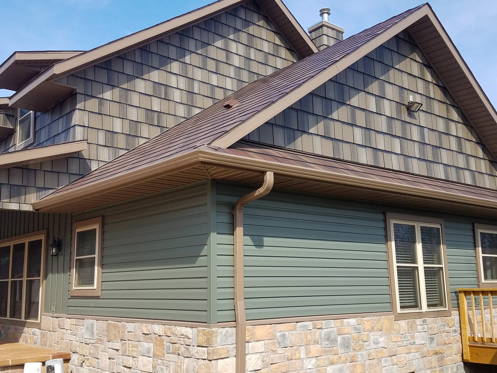A brown steel shake roof runs between two gables faced with weathered shake-look steel panels.