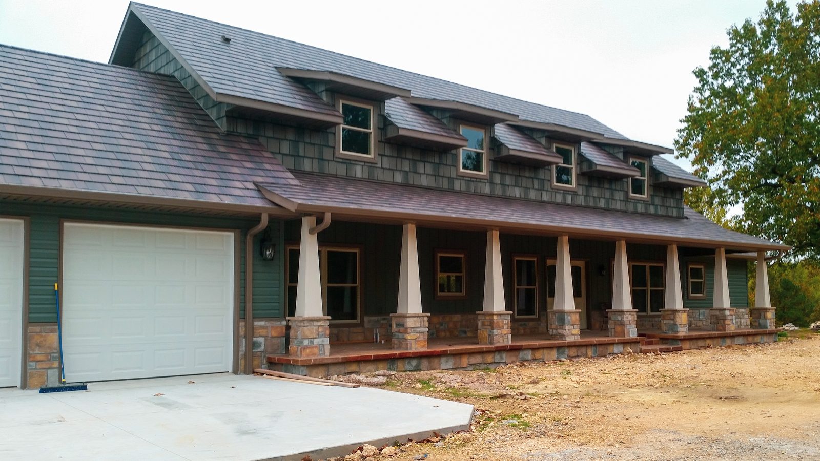 A row of dormers sits in brown steel shake roofing above a deep porch with tapered columns.