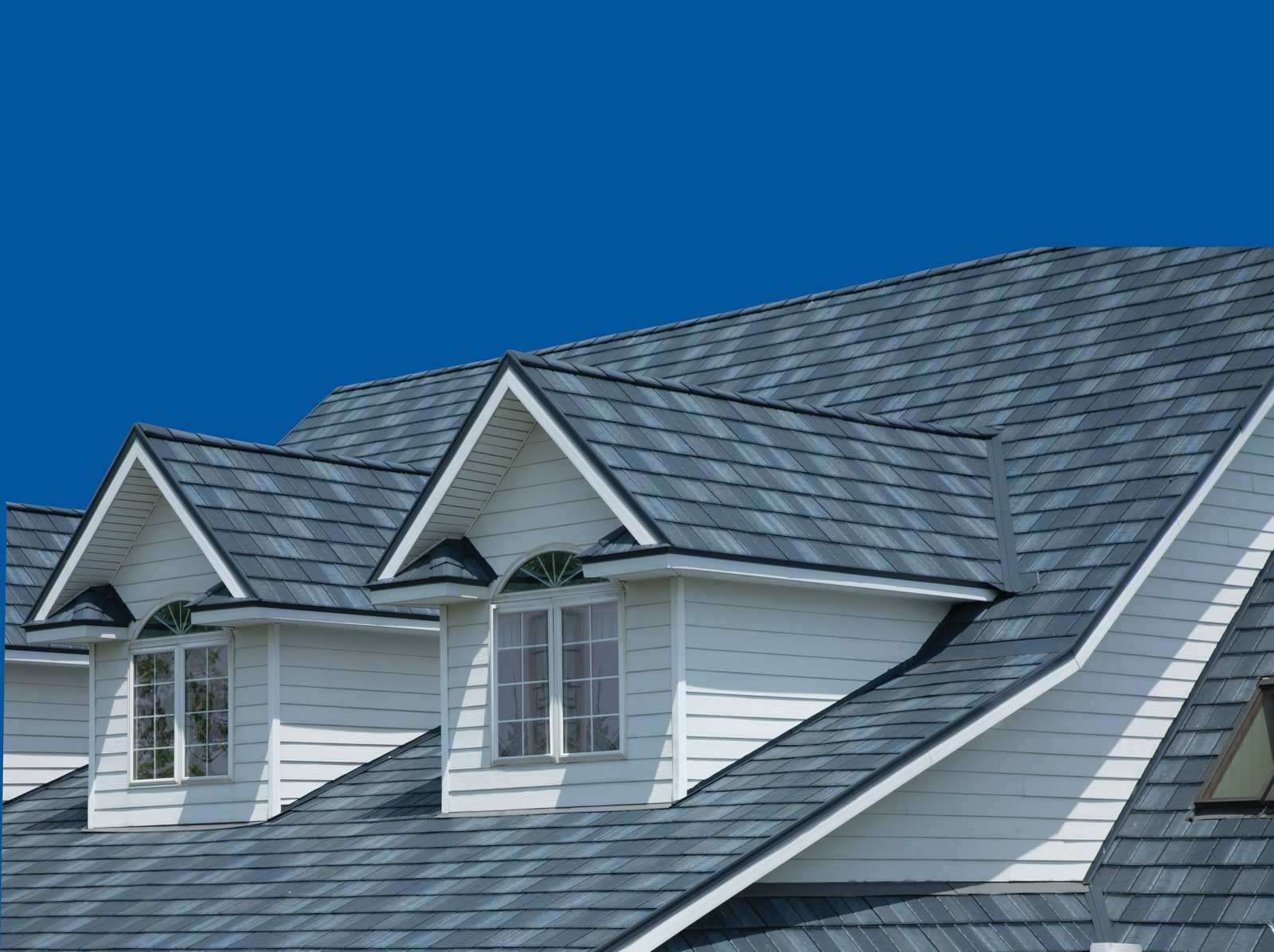 Gray-blue steel shake roofing surrounds two dormers above pale green-white lap siding.