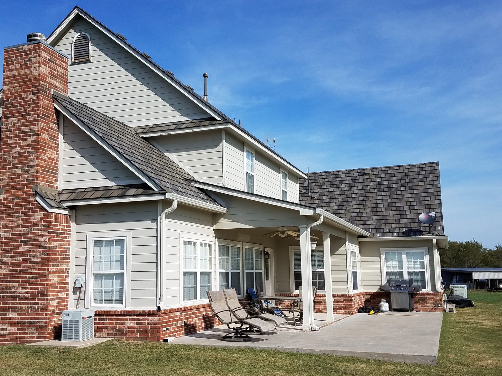 Rear elevation of a home combining a standing-seam porch roof with gray steel shake roofing above.