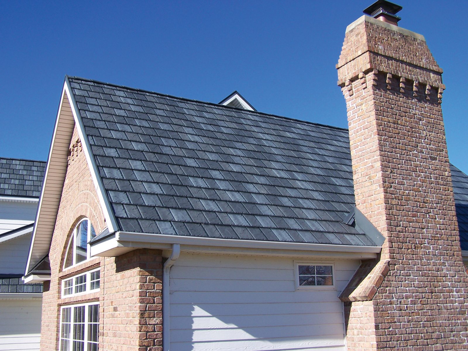 Dark slate-look steel roofing covers a steep gable beside a tall corbelled brick chimney.