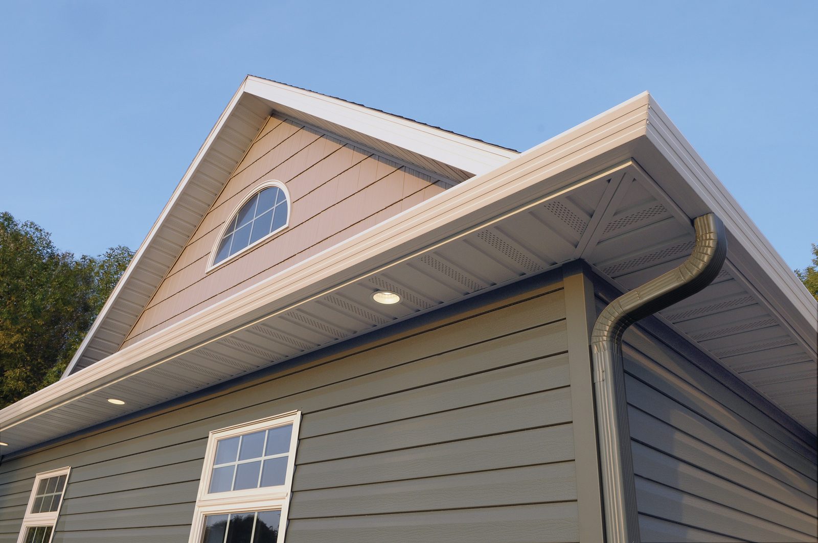 Sage lap siding rises to a gable with cream soffit, fascia, gutter and a rounded downspout elbow.