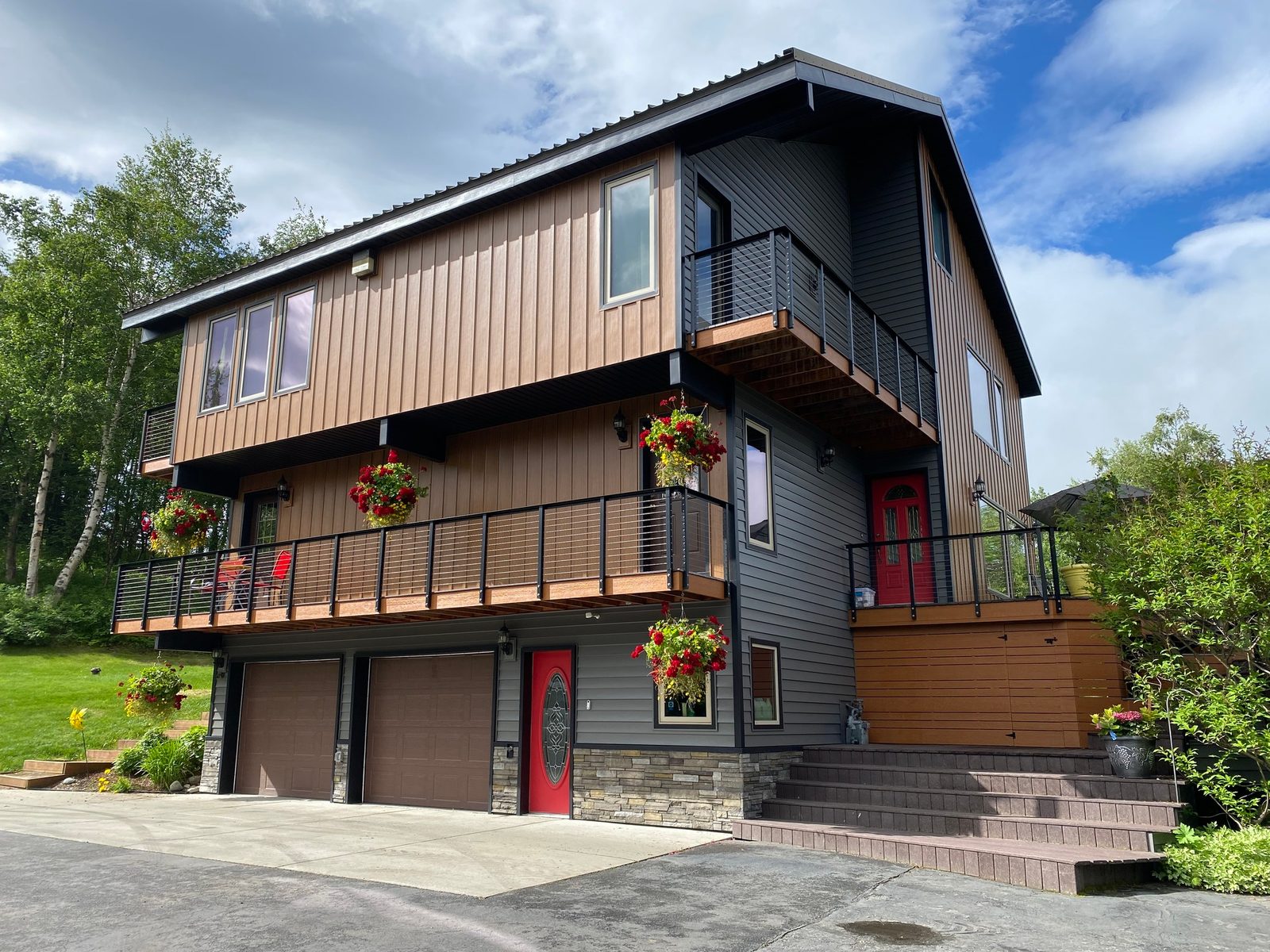 Charcoal and wood-look board-and-batten steel siding clad a three-level home with two tiered decks.