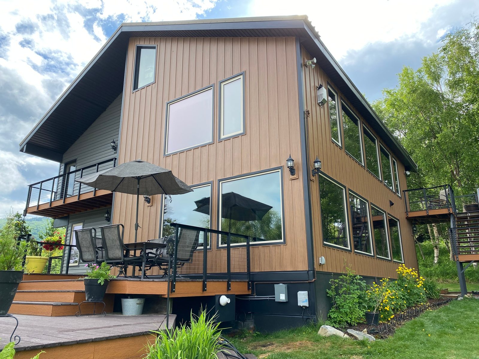 Wood-look vertical steel siding wraps a walkout elevation above a deck with a patio umbrella.