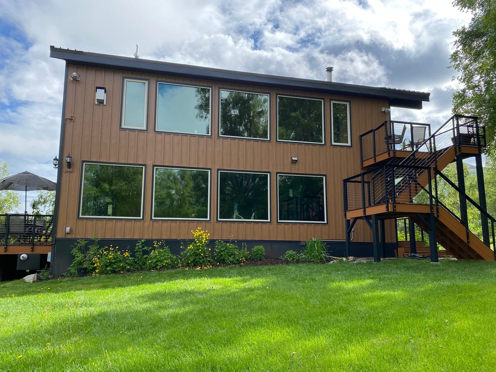 A tall rear elevation in wood-look vertical steel siding, with a black steel stair to an upper deck.