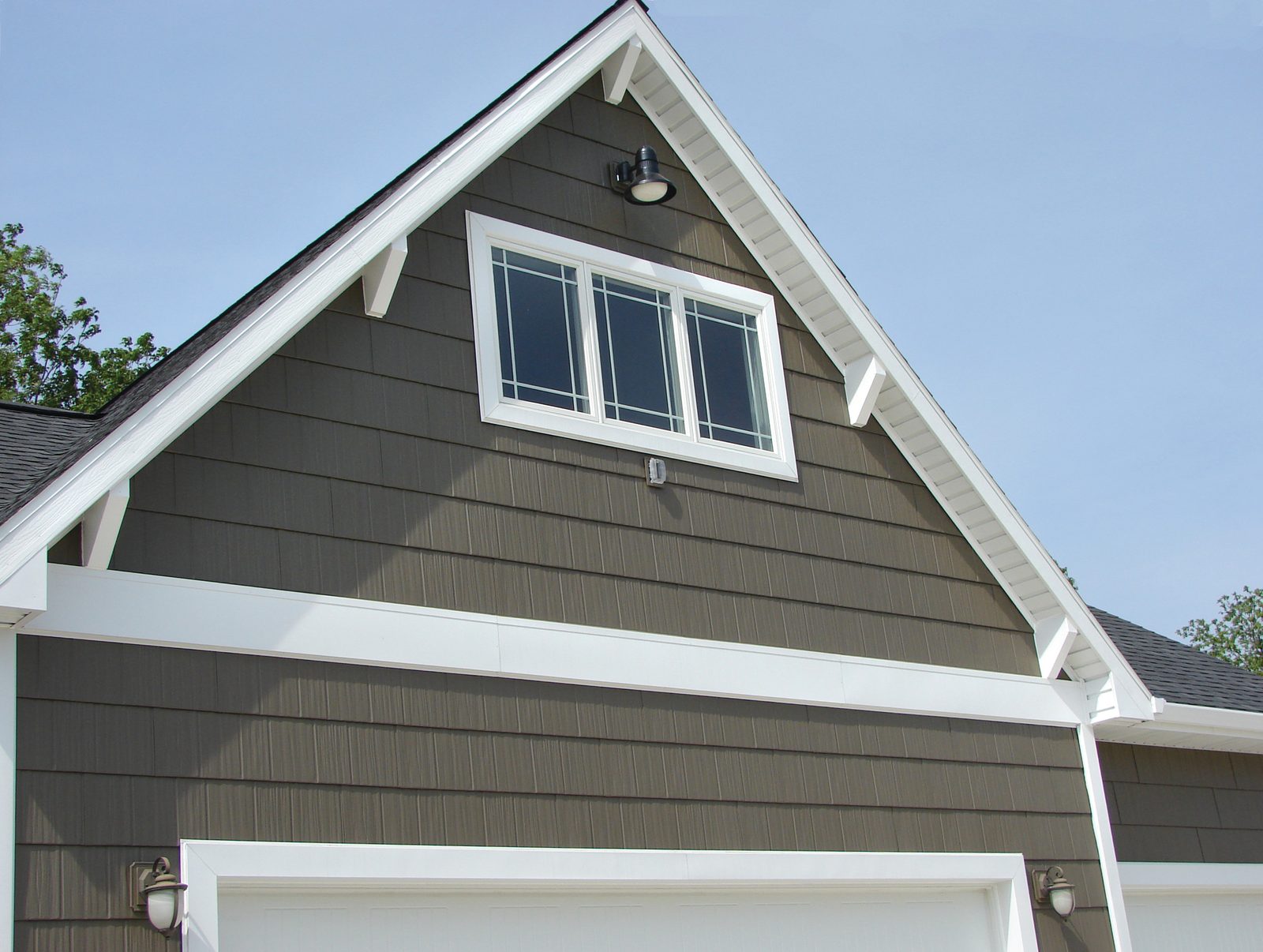 Charcoal shake-look steel siding fills a gable end above a garage, trimmed in white with brackets.