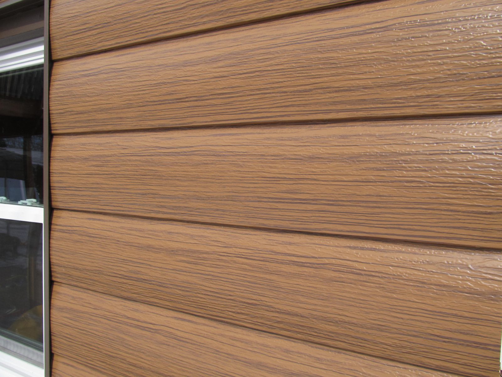 Close view of wood-look steel lap siding showing embossed grain across five courses.