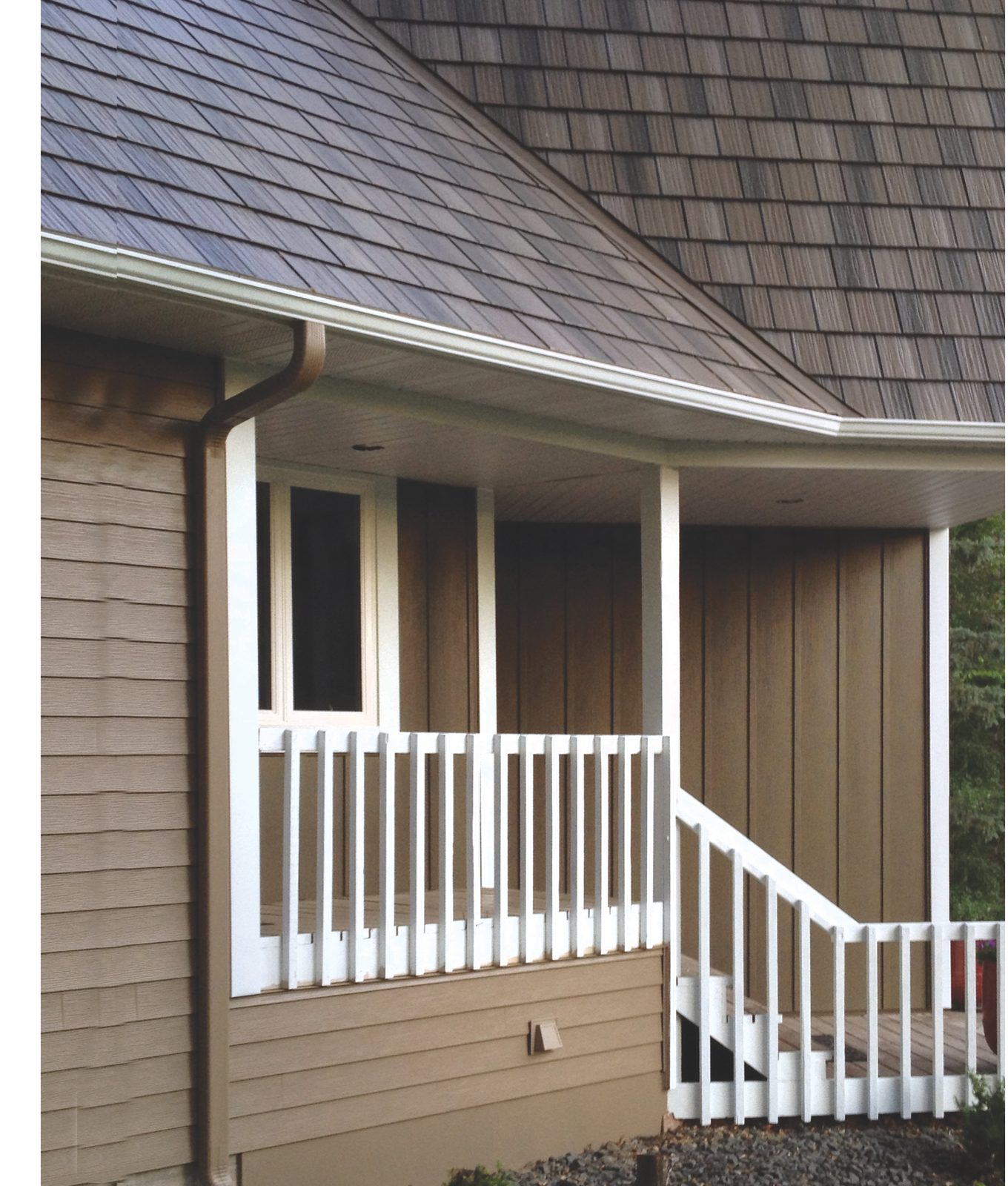 Tan lap siding and board-and-batten panels enclose a covered porch with a white rail and steps.
