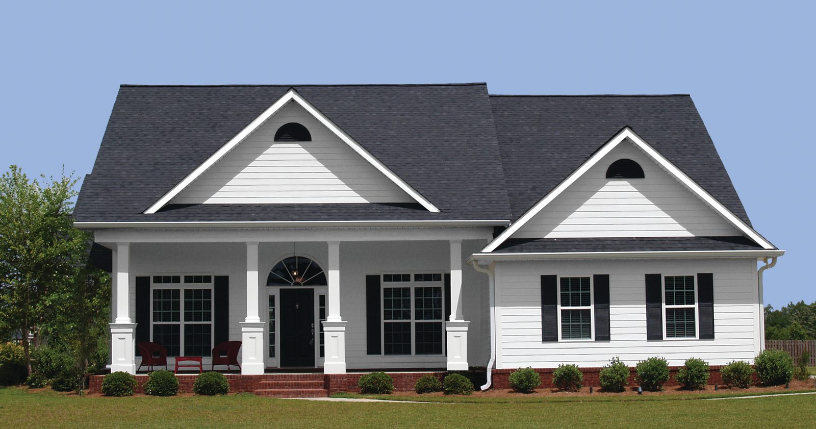 White lap siding and square columns front a single-story home with black shutters and gabled entries.