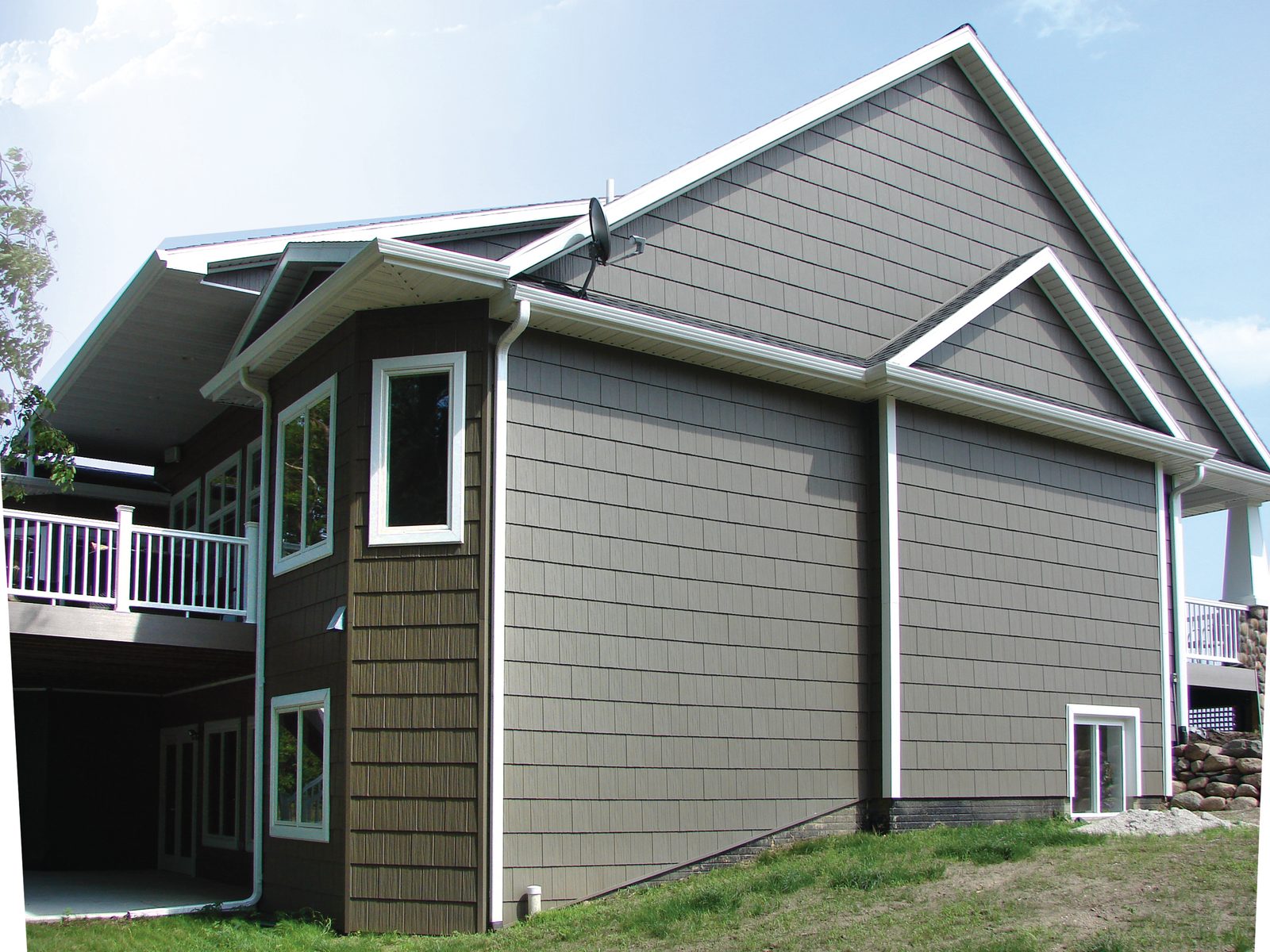 Sage shake-look steel siding fills a tall gable wall above lap siding and a walkout deck.