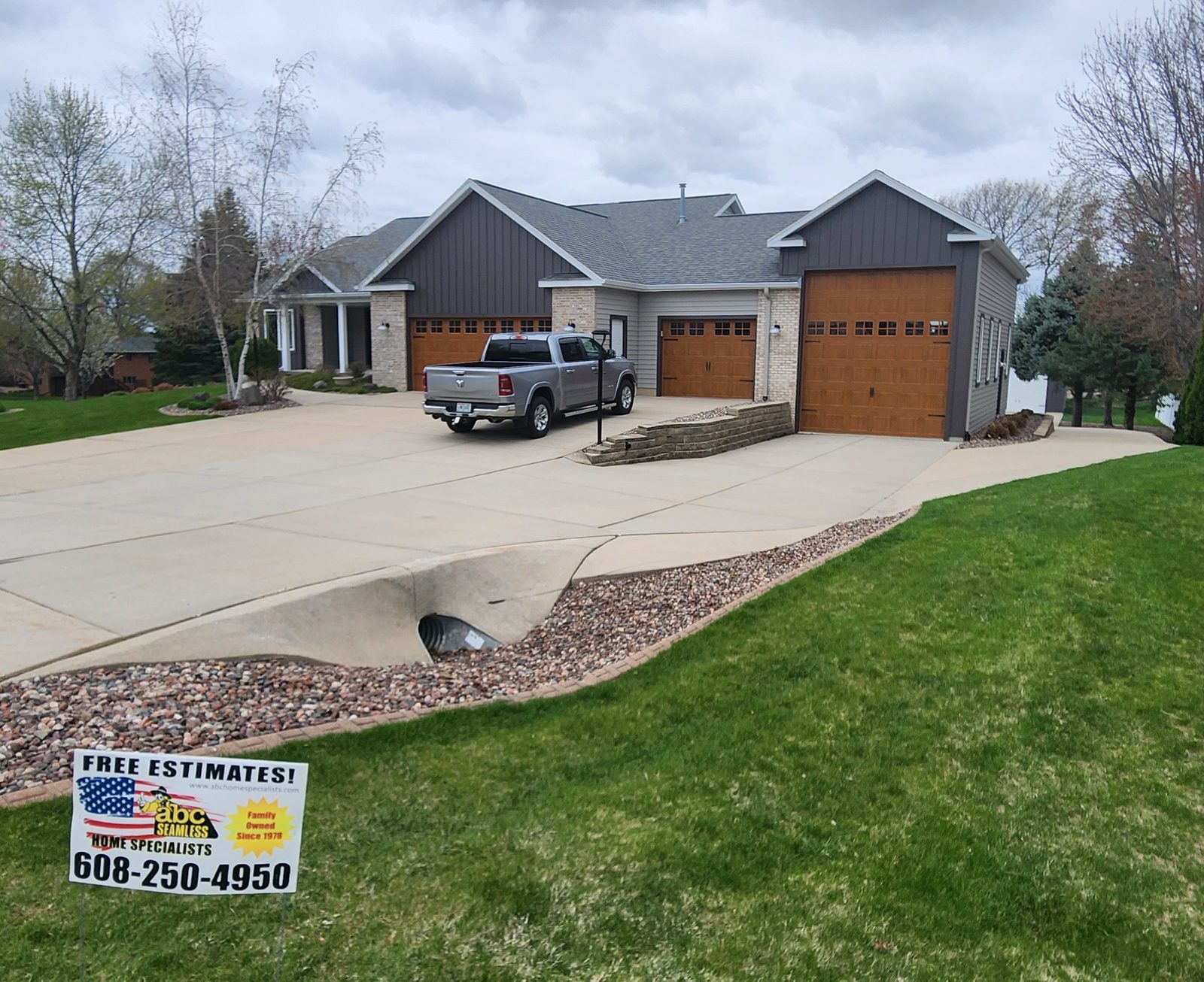 Gray lap siding and dark board-and-batten gables front a ranch home with three wood-tone garage doors.
