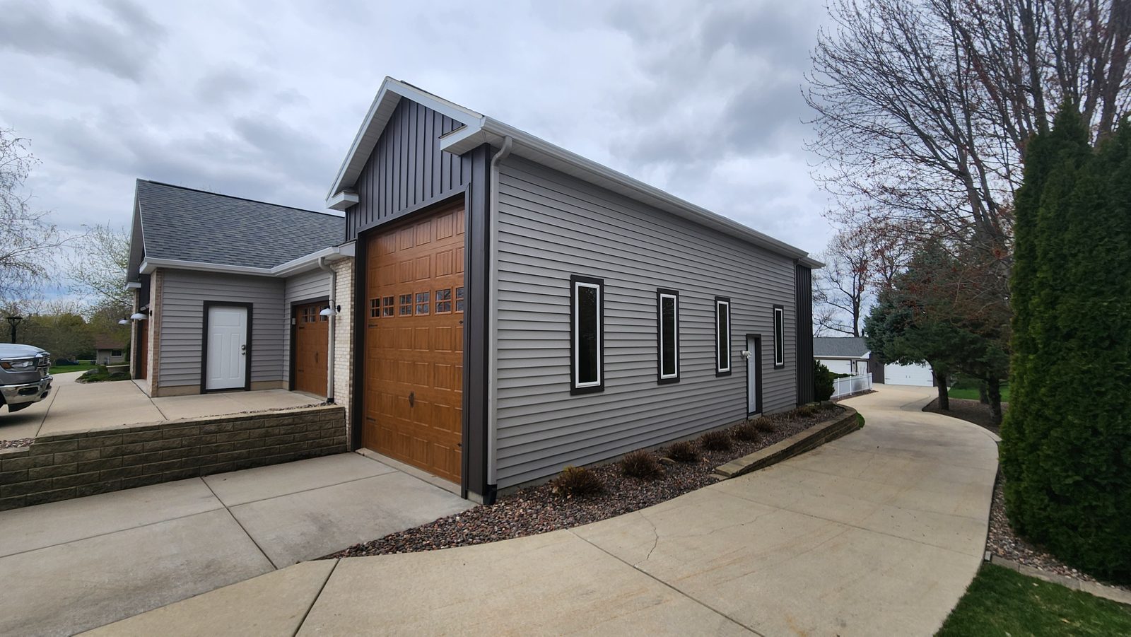 Gray lap steel siding wraps a garage wing with a dark board-and-batten gable and a wood-tone door.