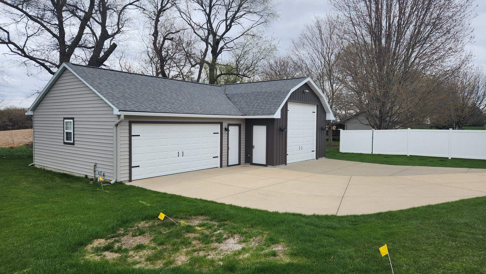 A detached garage in pale lap siding with a dark board-and-batten bay and three white doors.