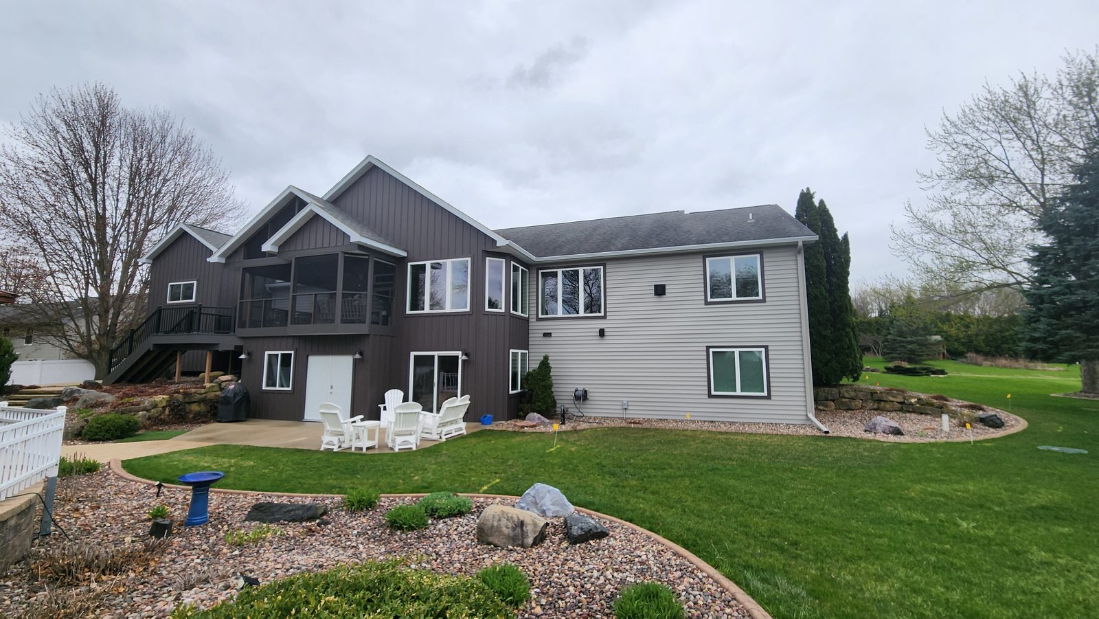 Dark board-and-batten and pale lap steel siding wrap a walkout rear elevation with a screened porch.